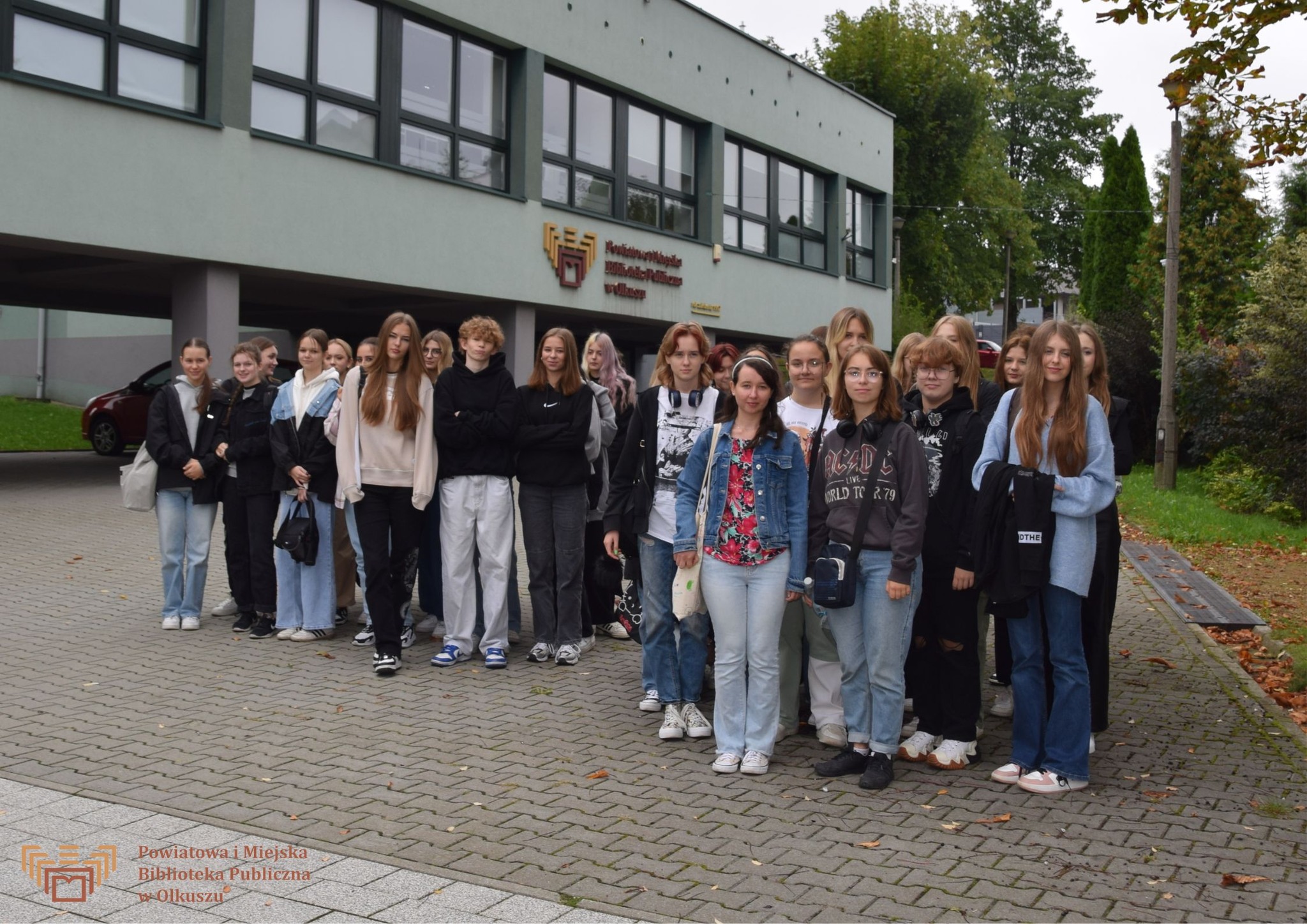 Zdjęcie zostało zrobione przed budynkiem olkuskiej Biblioteki. Przedstawia dużą grupę młodzieży, pozującą do wspólnego zdjęcia.